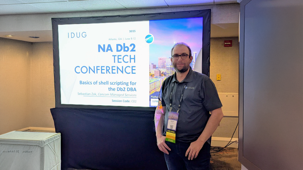 Sebastian steht vor einem großen Bildschirm, auf dem die erste Folie seines Vortrags auf der IDUG Konferenz zum Thema NA Db2 gezeigt wird.
