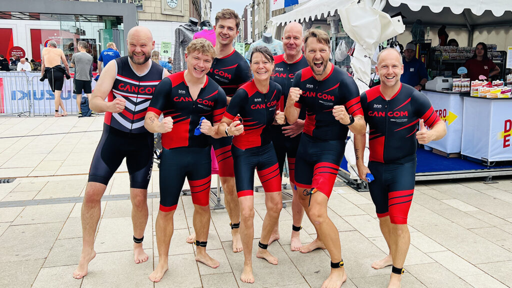 Gemeinsam an den Start: Das CANCOM Triathlon-Team 10 Das CANCOM Triathlon-Team steht in ihren Wettkampftrikots mit kämpferischen Posen zusammen.