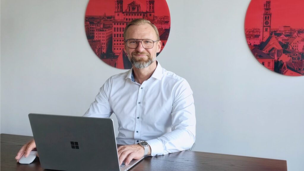 20 Jahre bei CANCOM: Vom leidenschaftlichen Gamer zum Director einer ganzen Region 28 Sascha sitzt in einem Meetingraum mit Laptop und Computermaus. Er trägt ein weißes Hemd und eine Brille.