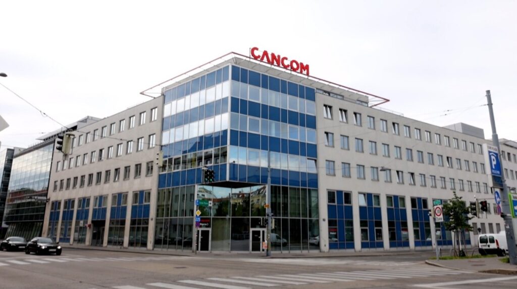 Auf dem Bild ist das CANCOM Gebäude in Wien zu sehen. Es ist sehr modern mit einer Glasfront. Auf dem Dach ist das CANCOM Logo zu sehen.
